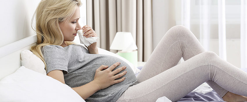 Pregnant woman with allergy sitting on bed at home