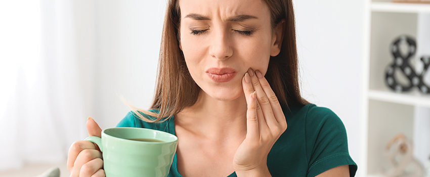 Young woman with sensitive teeth and cup of hot coffee at home