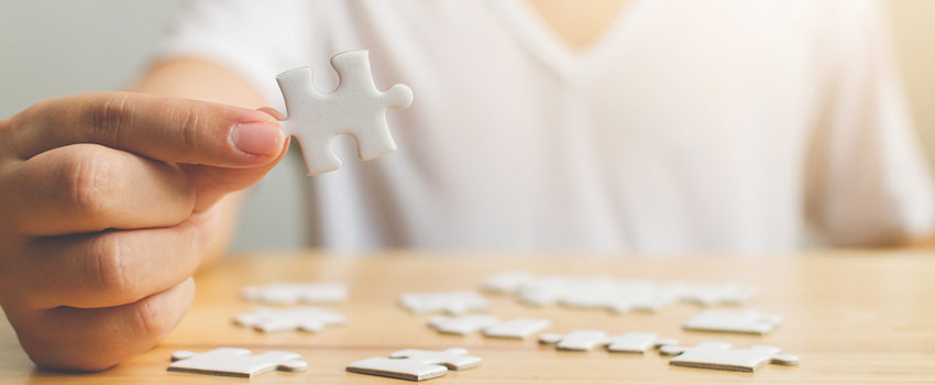 Hand of male trying to connect pieces of white jigsaw puzzle on wooden table. Healthcare for alzheimer disease, dementia, memory loss, autism awareness and mental health concept