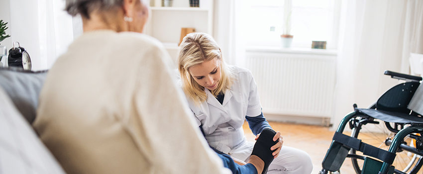 A health visitor putting on slippers on a senior woman at home.