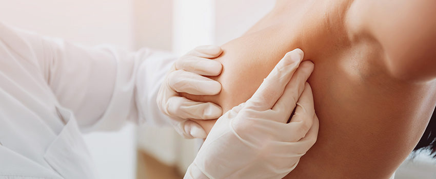 Doctor get examining breast of young woman. Consultation with gynecologist.