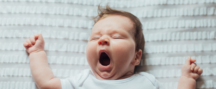 Infant baby sleeping and yawning on white sheets