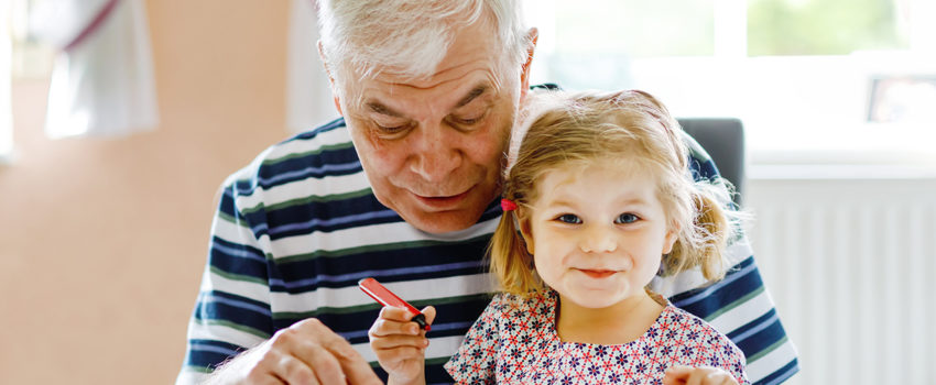 Cute little baby toddler girl and handsome senior grandfather painting with colorful pencils at home. Grandchild and man having fun together